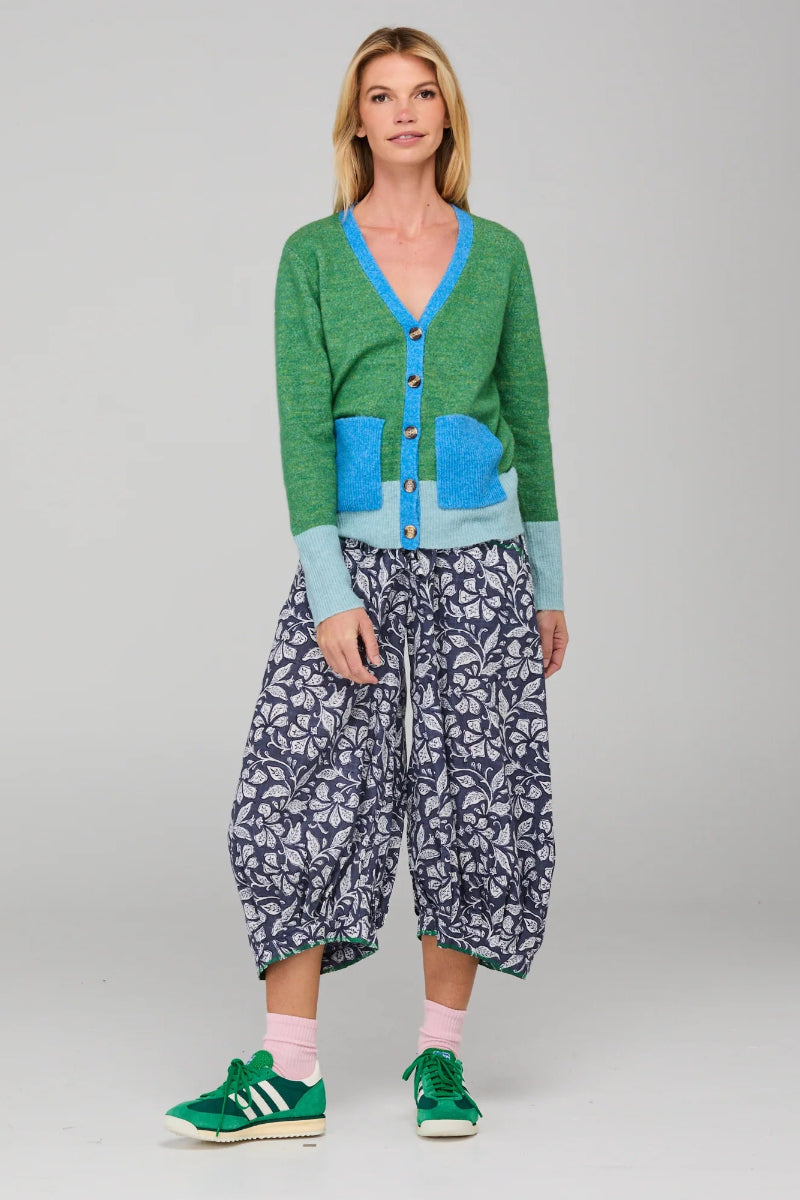 Woman wearing a green cardigan, blue shirt, and patterned pants on a gray background