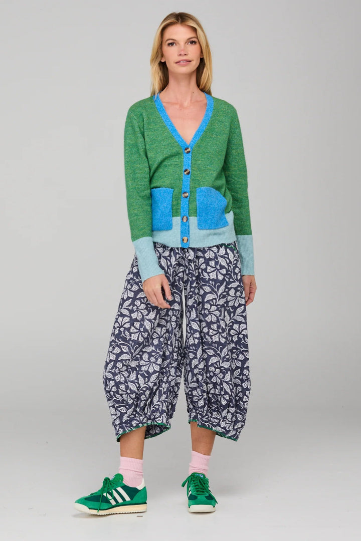 Woman wearing a green cardigan, blue shirt, and patterned pants on a gray background