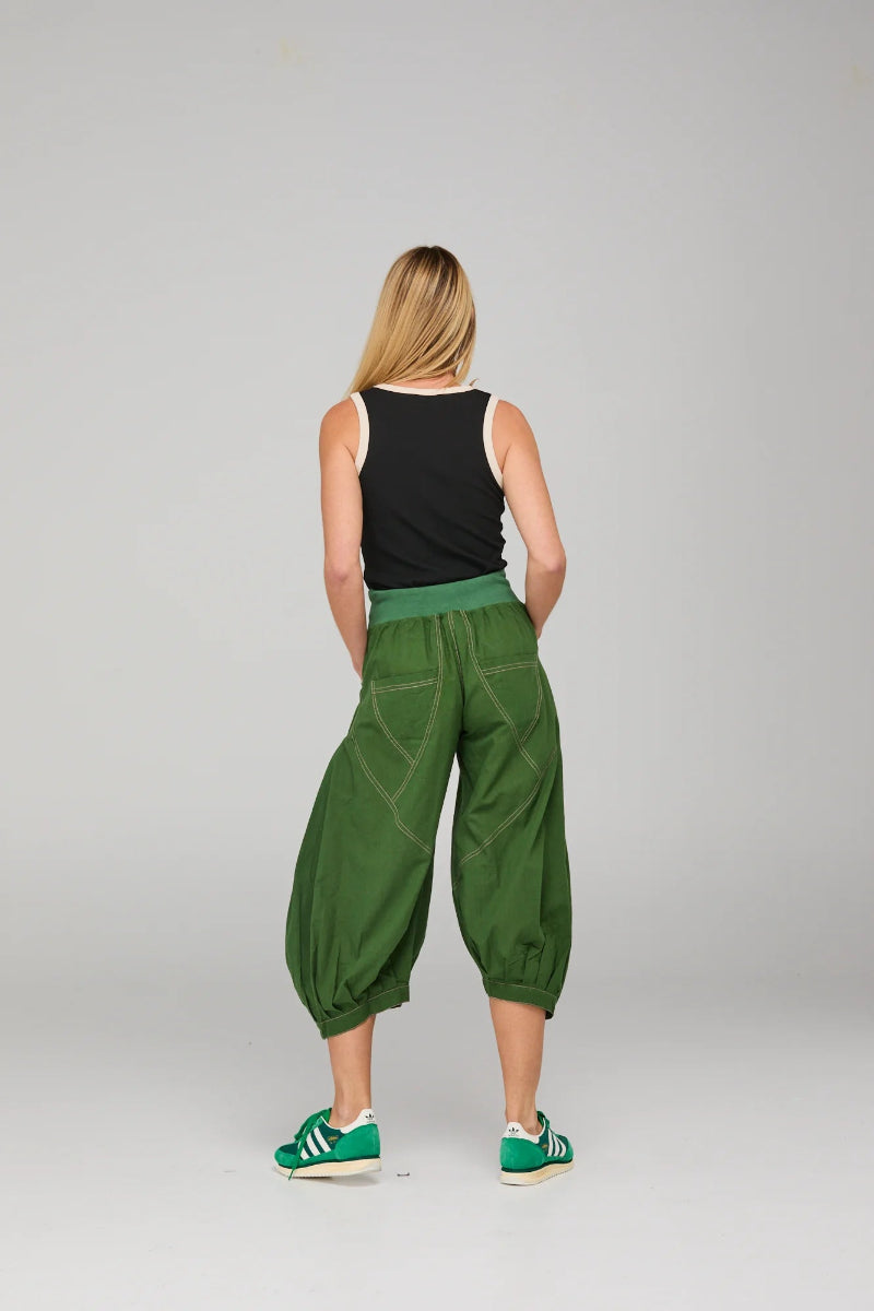 Person wearing green baggy pants and black top on a plain background