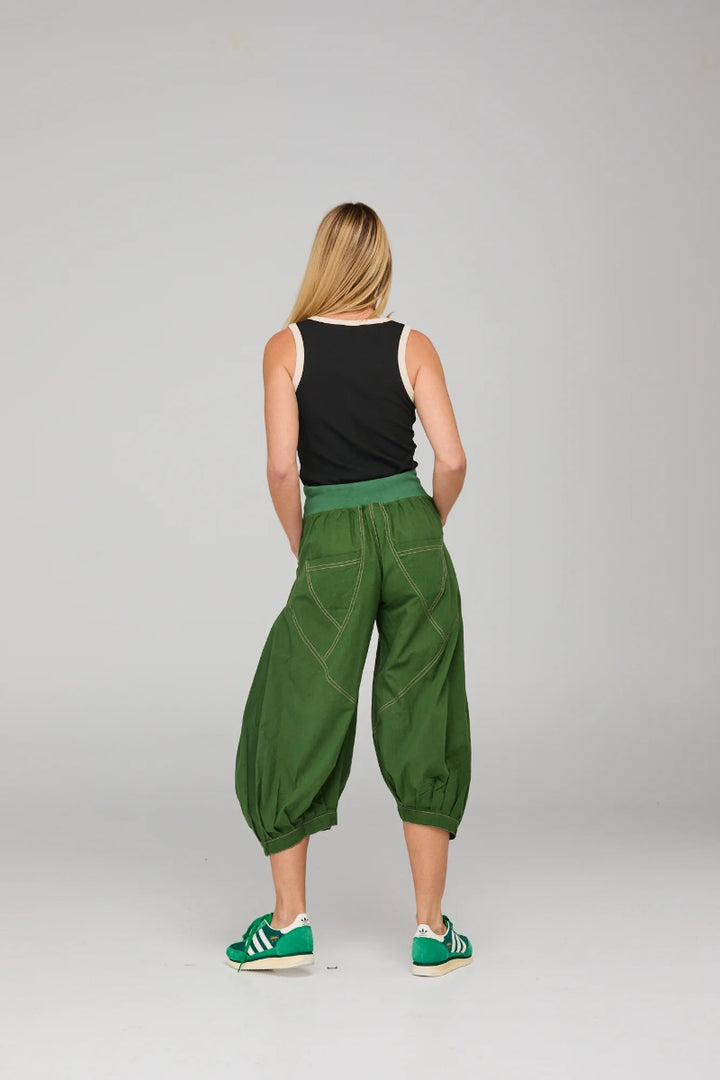 Person wearing green baggy pants and black top on a plain background