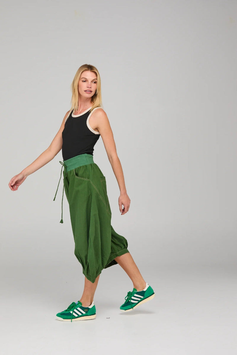 Woman wearing a black tank top and green wide-leg pants with green sneakers on a white background
