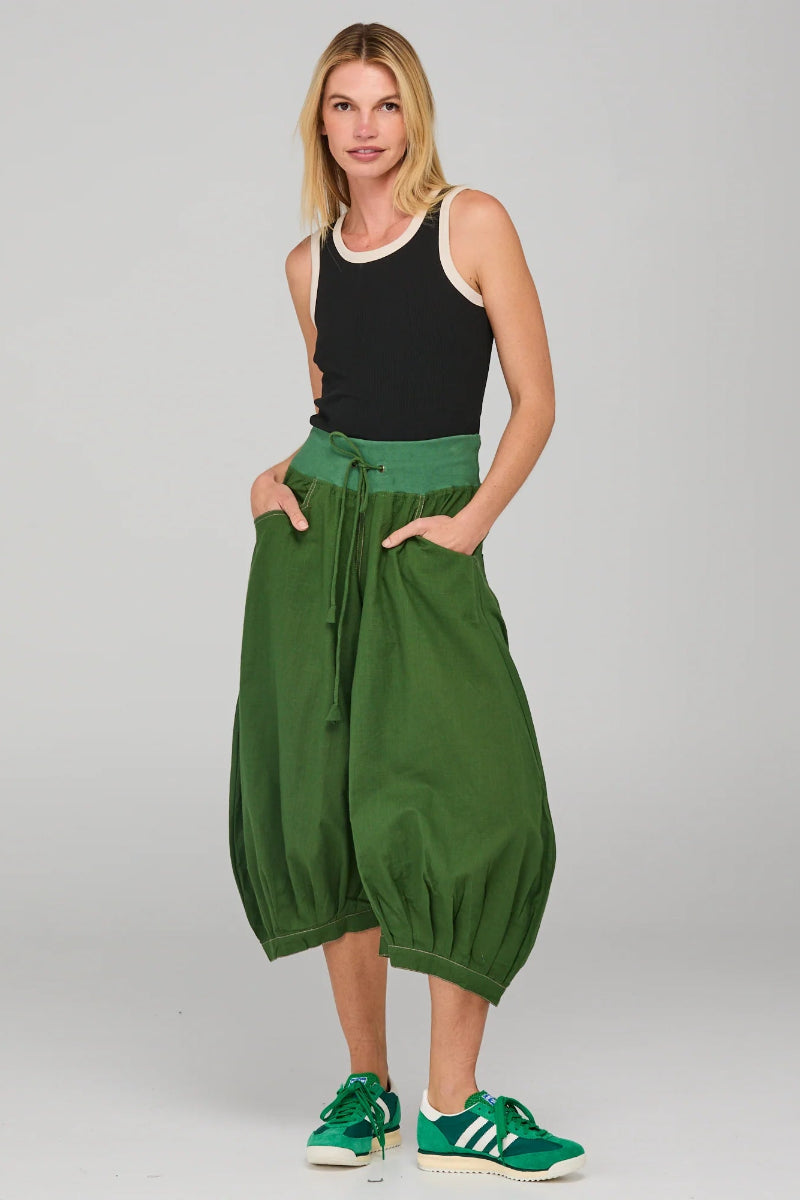 Woman wearing green wide-leg pants and black tank top on a gray background