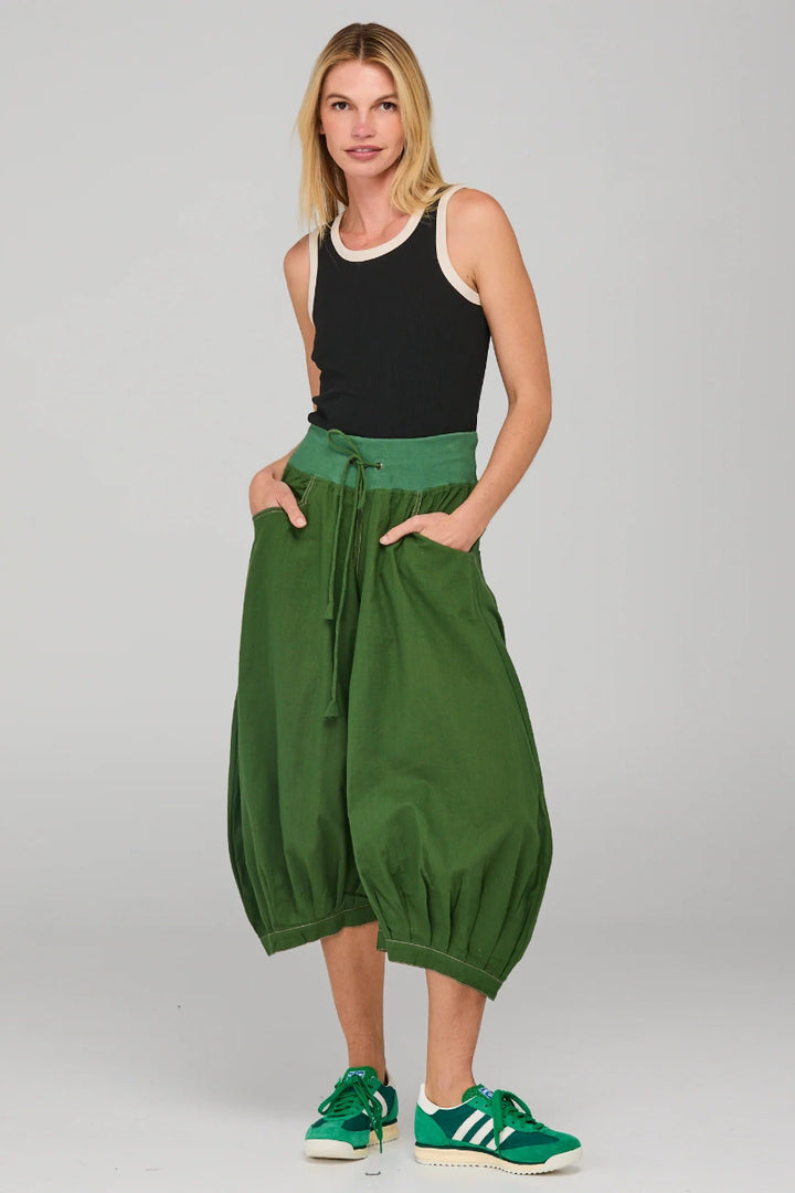 Woman wearing green wide-leg pants and black tank top on a gray background