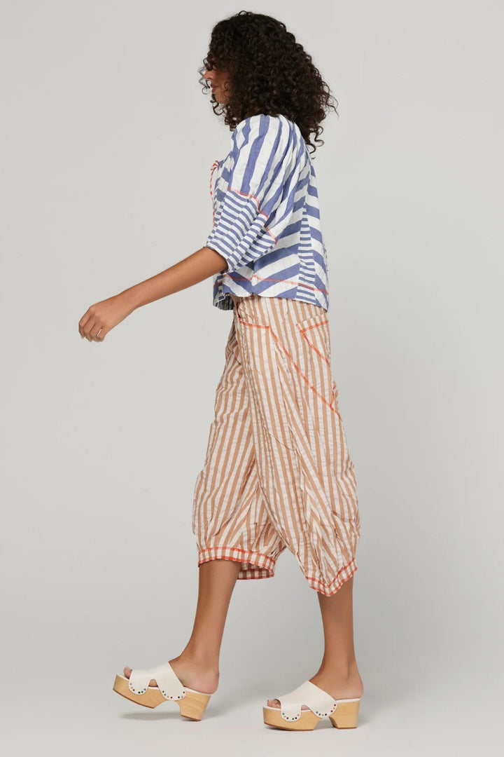 A woman is shown from the back wearing a blue and white striped shirt and peach and white striped wide-leg cropped pants, paired with white platform slide sandals, against a light gray studio background.