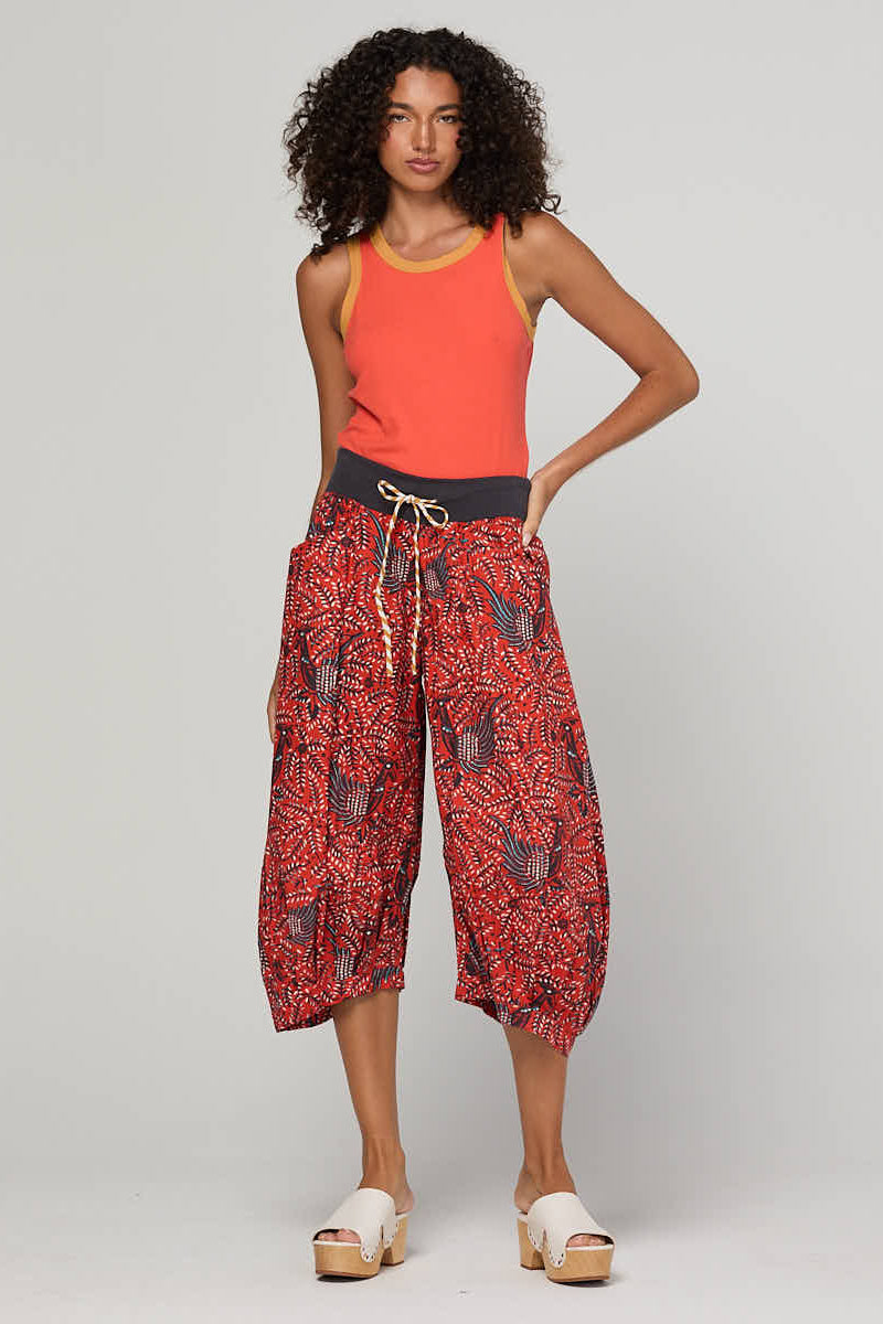 Woman wearing a red tank top and patterned red and black pants on a white background