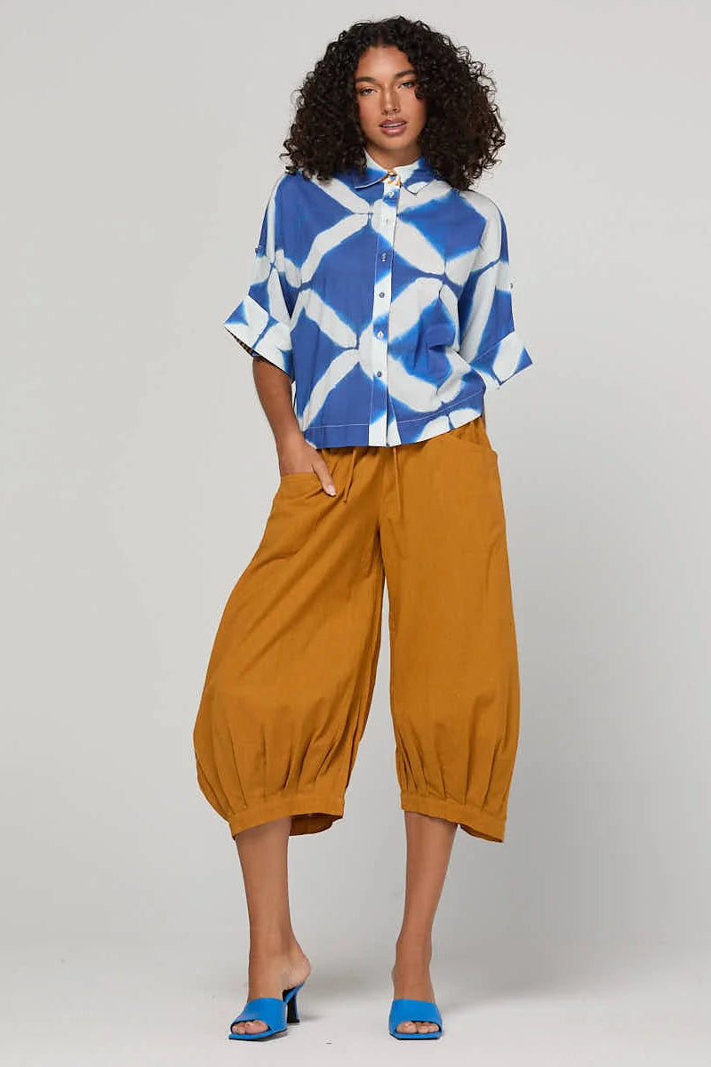 Woman wearing a blue and white patterned top with mustard yellow pants on a plain background