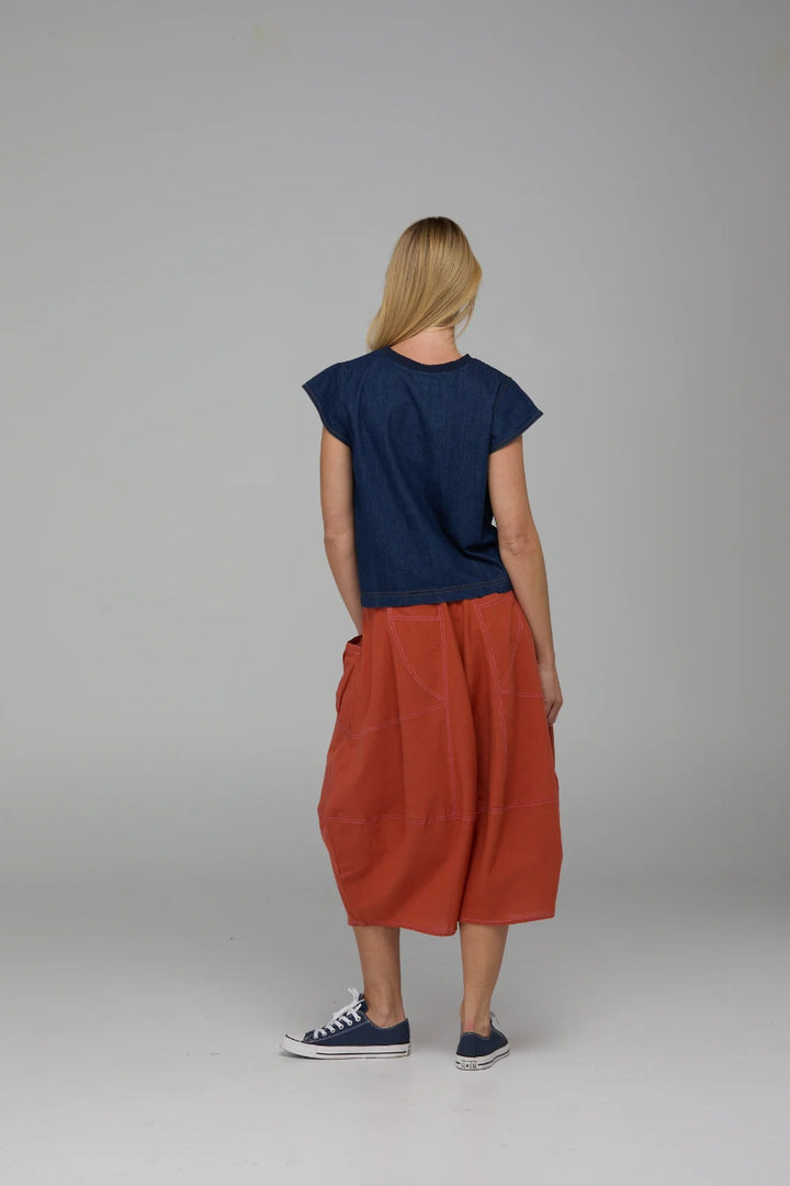 Person wearing a navy top and rust-colored pants on a plain background