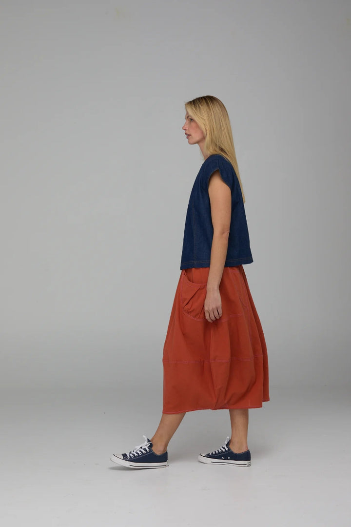 Woman wearing a navy top and rust-colored skirt on a gray background