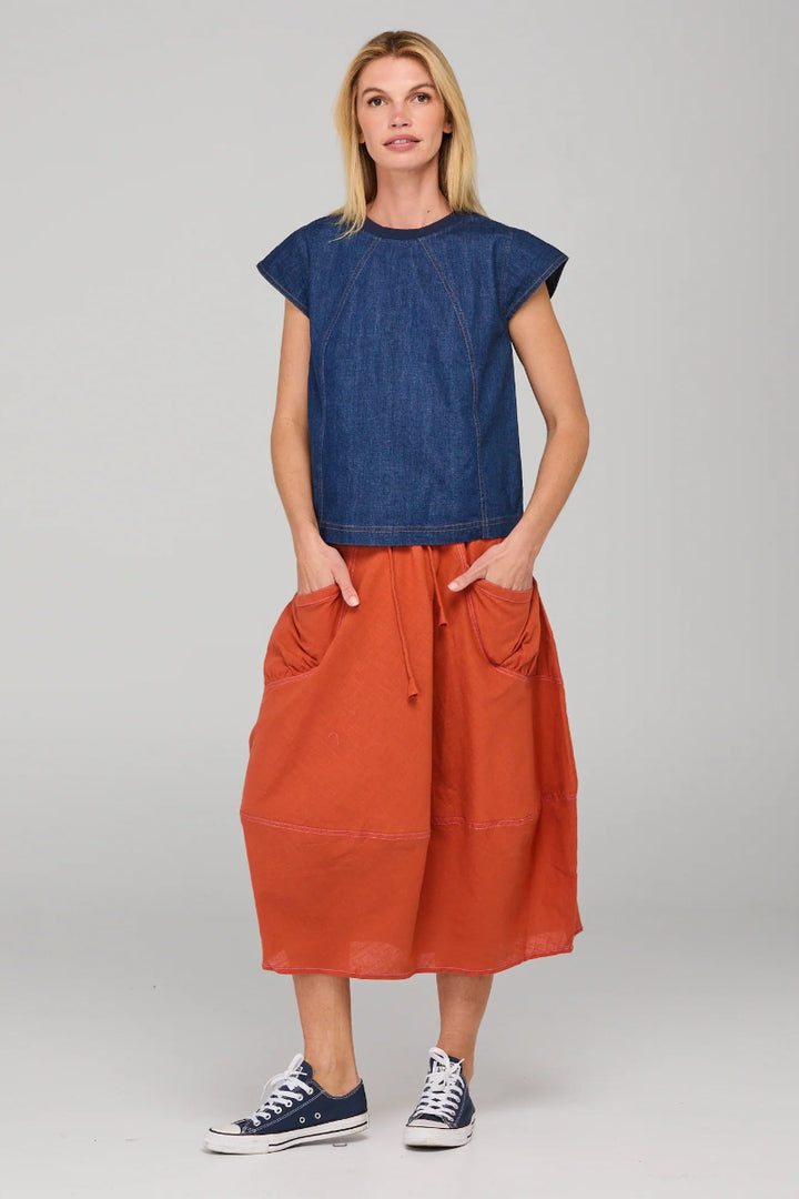 Woman wearing a blue top and orange skirt on a gray background