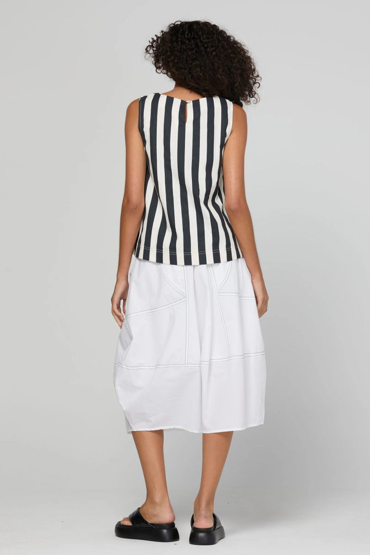 A woman shown from the back wearing a sleeveless black and white vertically striped top paired with a white midi skirt and black platform sandals, against a light gray studio background.