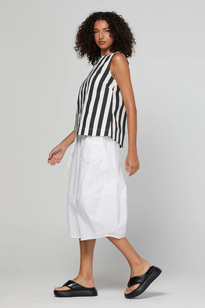 A model wearing a sleeveless black and white striped crop top, a white midi skirt, and black platform sandals, photographed against a light gray studio background.