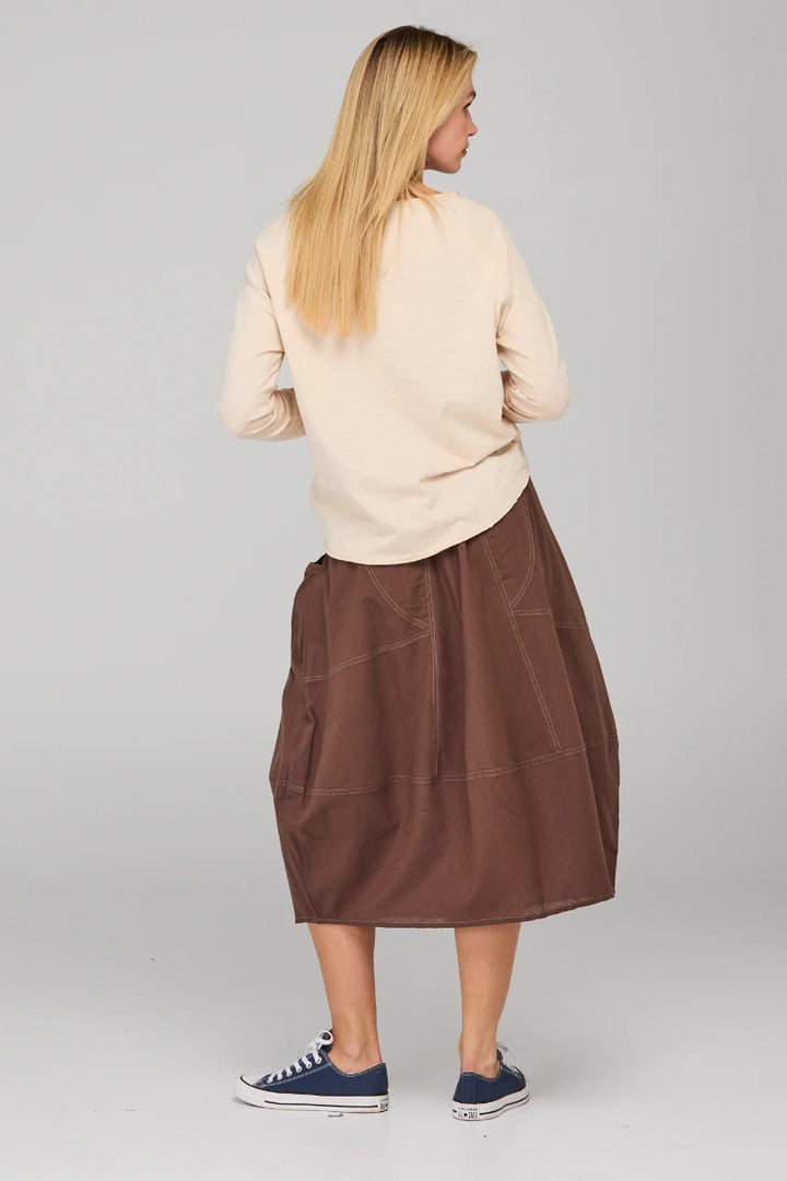 Person wearing a beige sweater and brown skirt on a plain background