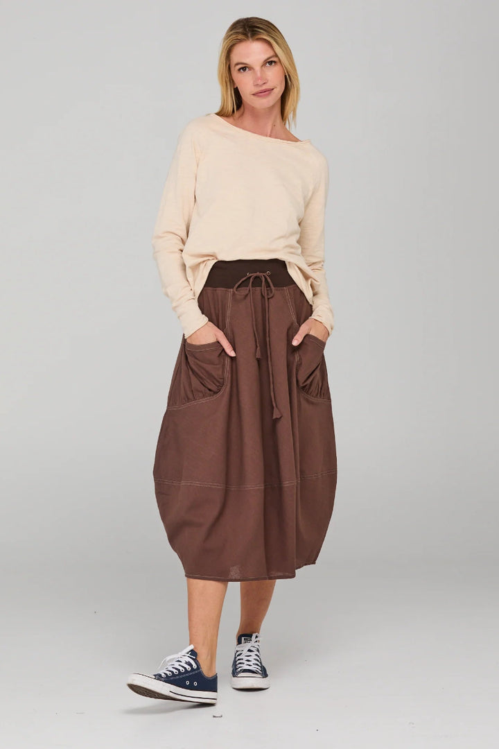 Woman wearing a beige sweater and brown skirt on a plain background