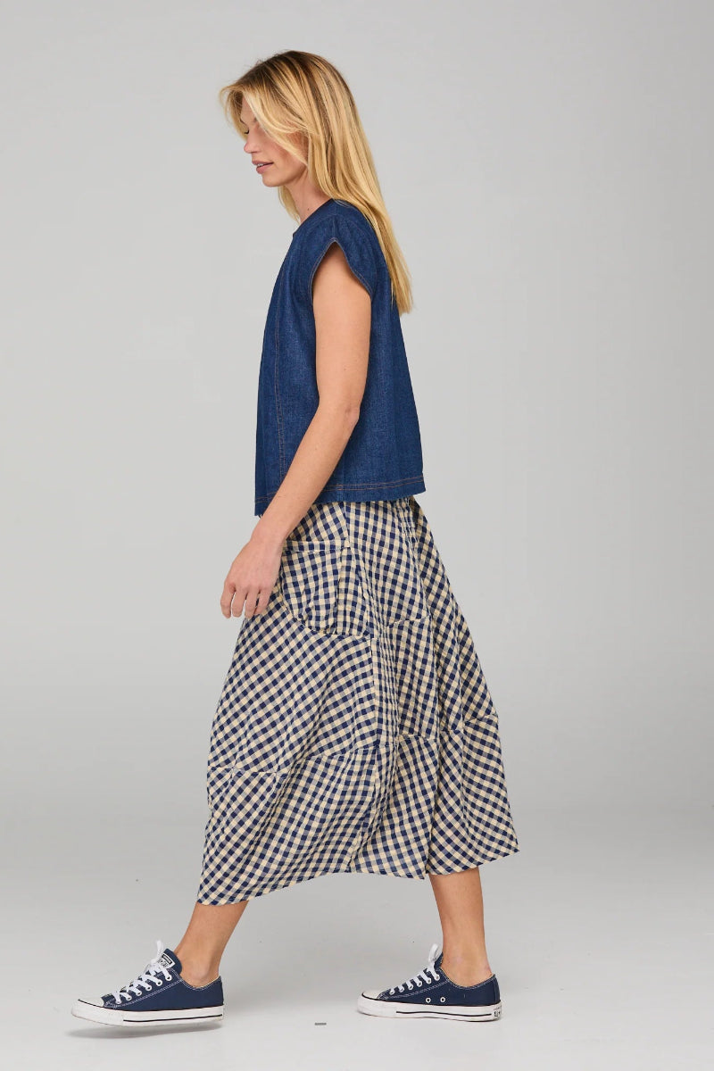 Woman wearing a blue sleeveless top and checkered skirt on a plain background