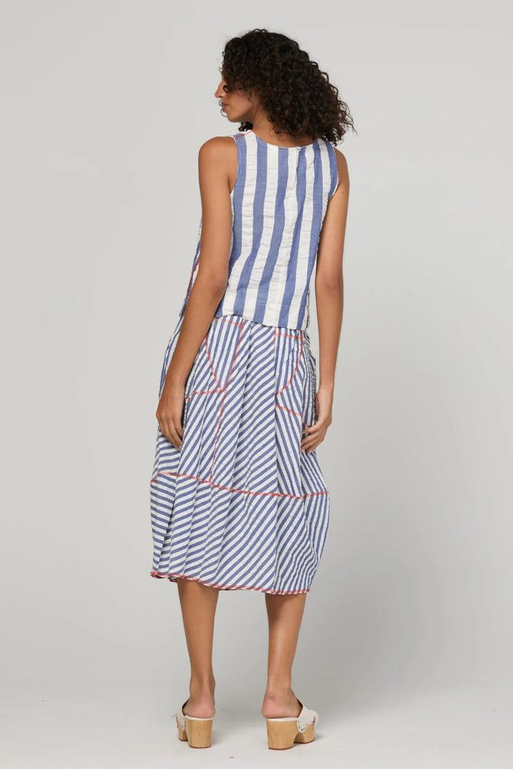 A woman viewed from the back wearing a sleeveless midi dress with vertical blue and white stripes on the bodice and diagonal blue and white stripes with thin red lines on the skirt, paired with beige platform sandals, against a light gray studio background.