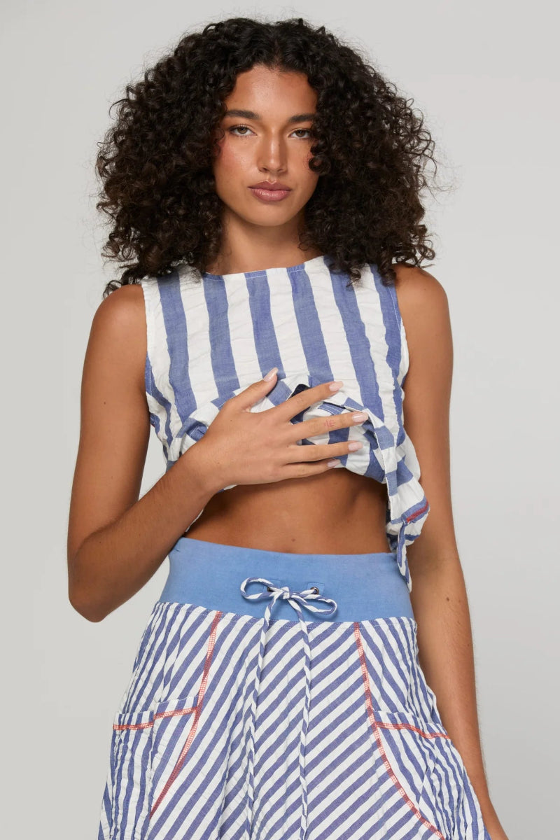 A model with curly dark hair wearing a blue and white striped sleeveless crop top and matching striped high-waisted shorts with a solid blue waistband.