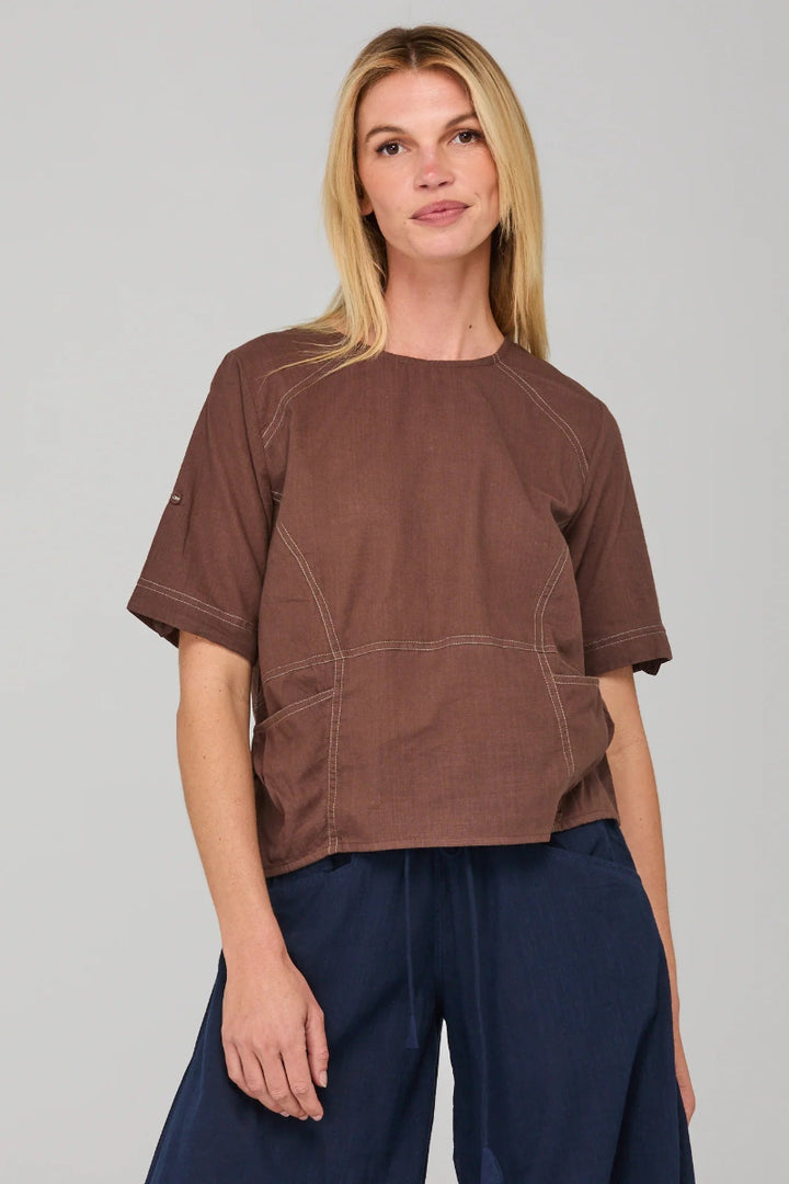 Woman wearing a brown t-shirt with a pocket design on a gray background