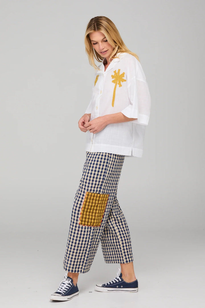 Woman wearing a white shirt with a palm tree design and checkered pants on a gray background