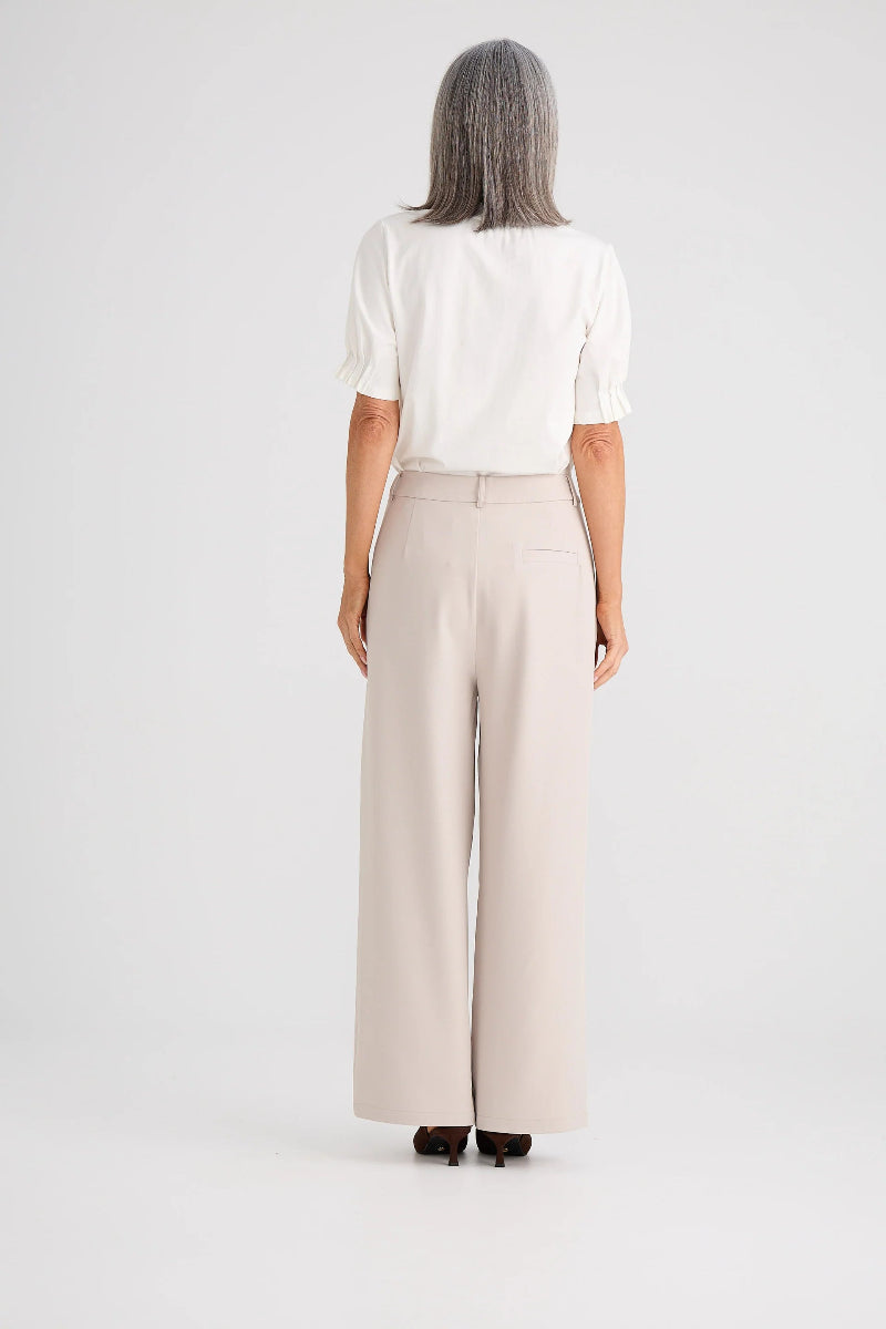 Person wearing a white blouse and beige wide-leg pants on a plain background