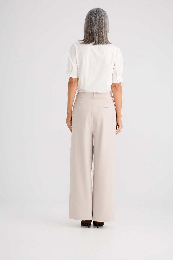 Person wearing a white blouse and beige wide-leg pants on a plain background