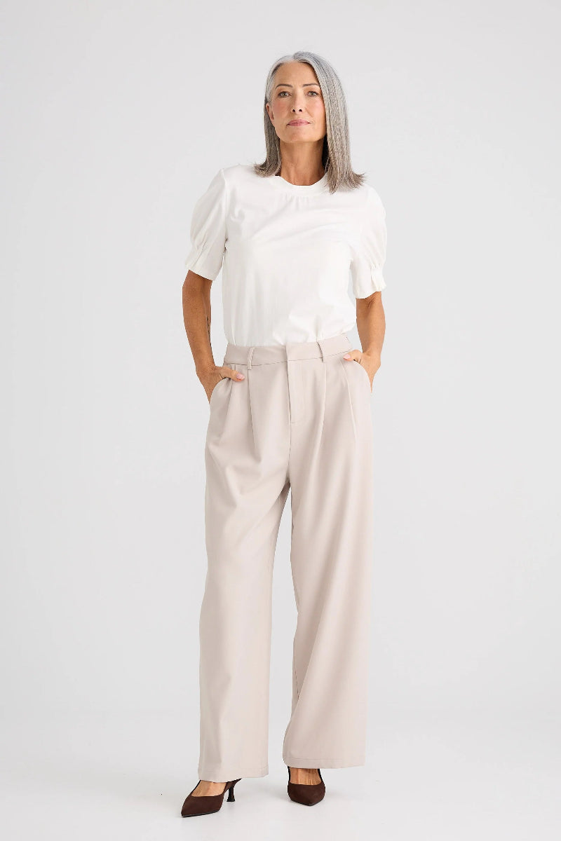 Woman wearing a white top and beige pants on a plain background