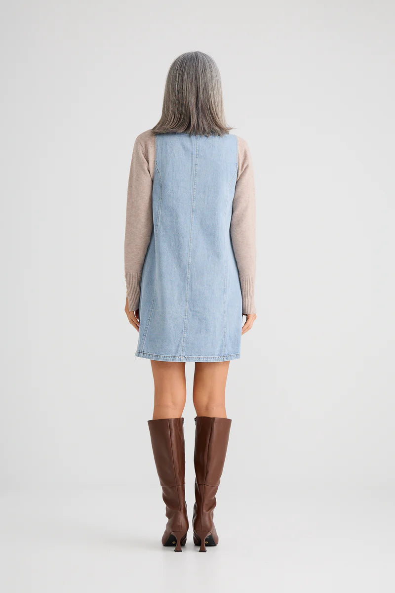 Person wearing a light blue denim dress with brown knee-high boots on a white background