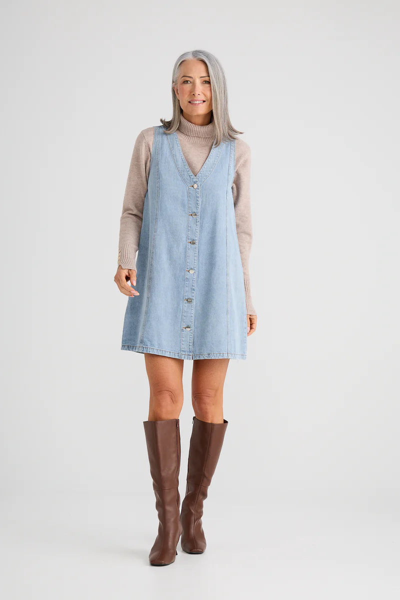 Woman wearing a light blue denim dress with a beige long-sleeve shirt and brown knee-high boots on a white background