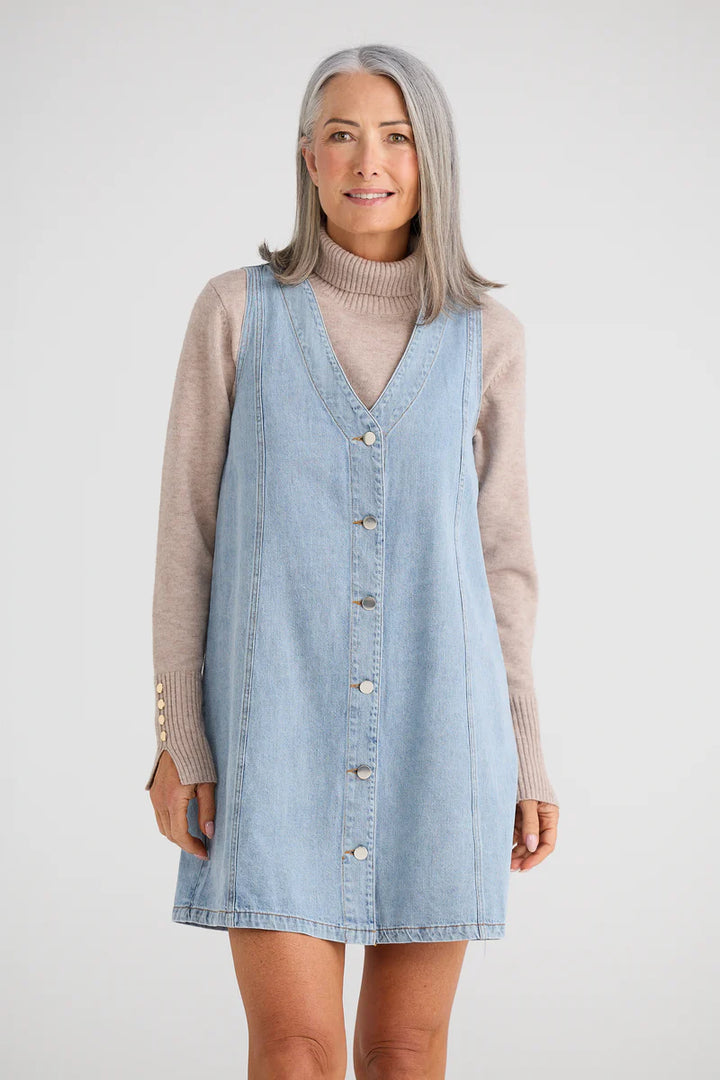 Woman wearing a light blue denim dress over a beige sweater on a white background
