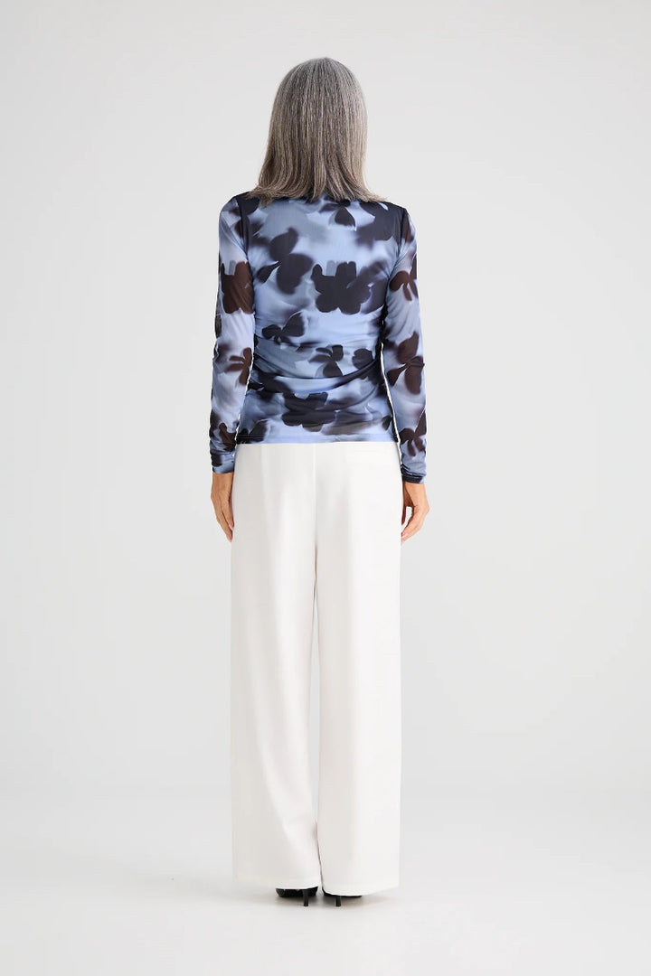 Person wearing a patterned long-sleeve top and white pants on a plain background