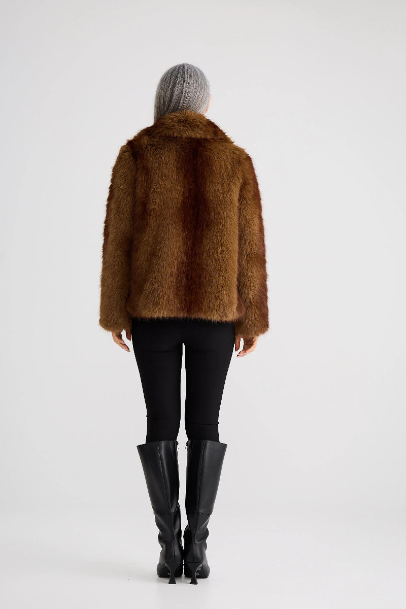 Person wearing a brown fur coat and black leggings on a white background