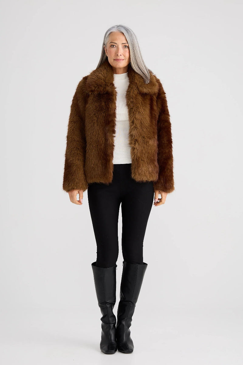 Woman wearing a brown faux fur jacket, black leggings, and black boots on a white background