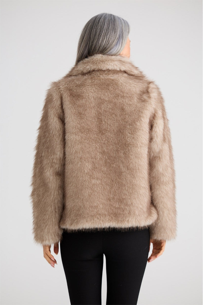 Person wearing a beige faux fur jacket on a plain background