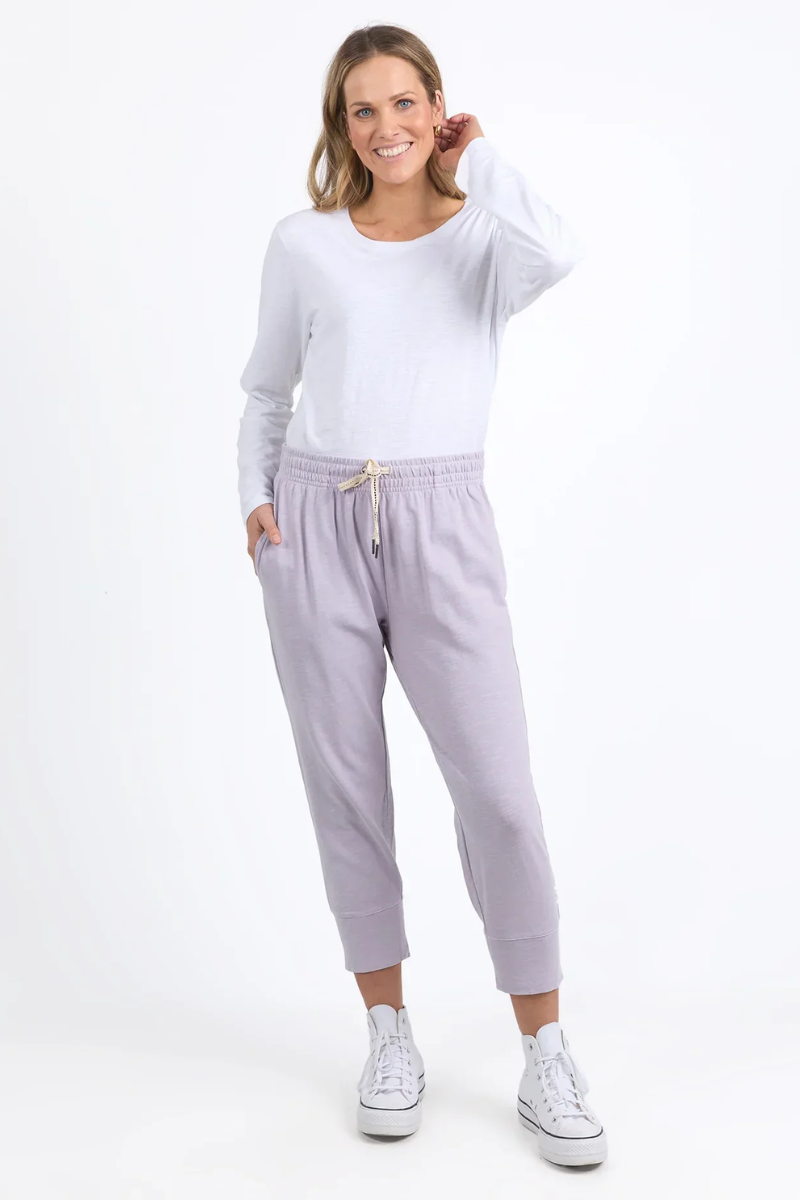 Woman wearing a white long-sleeve top and light purple sweatpants on a white background