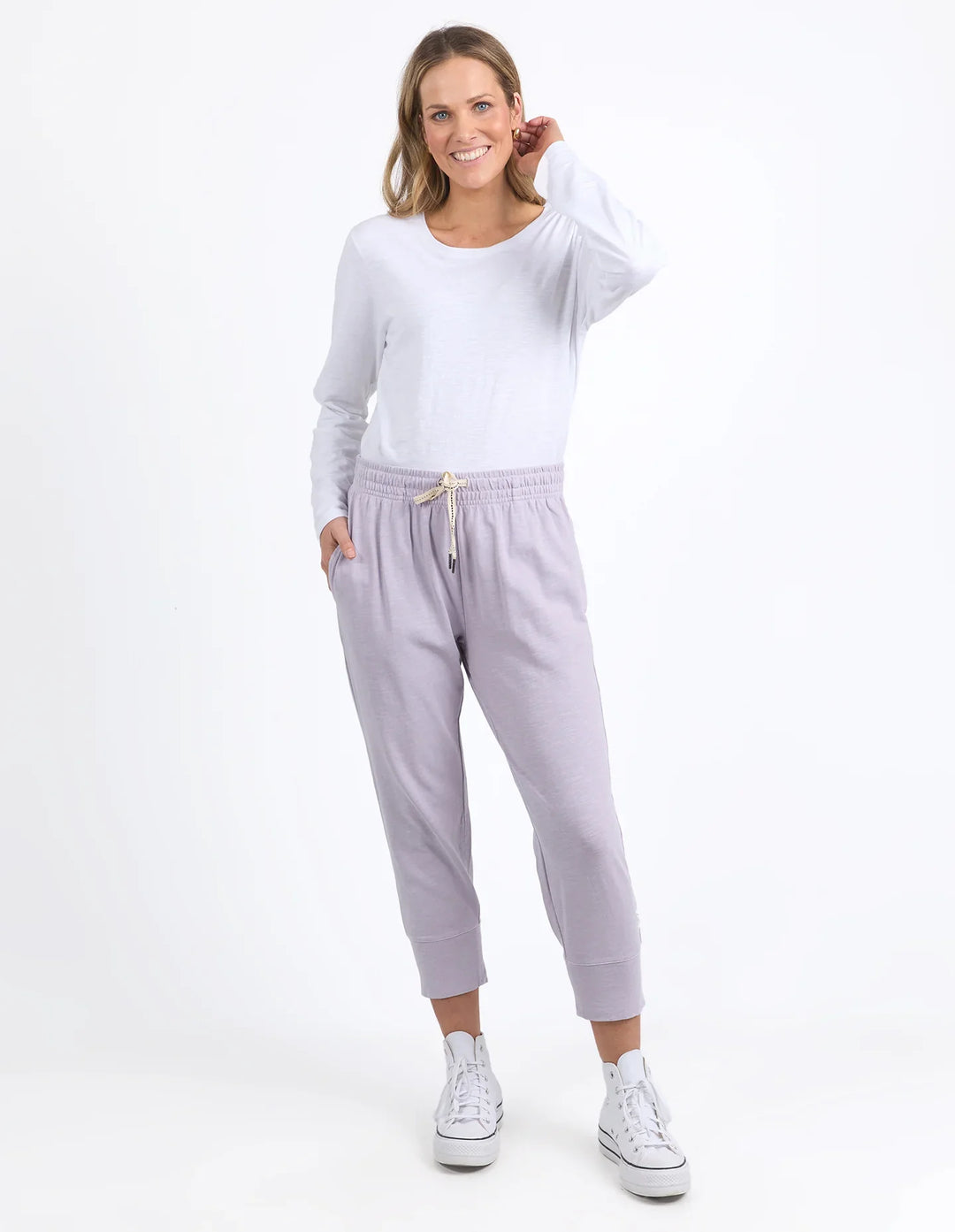 Woman wearing a white long-sleeve top and light gray sweatpants on a white background