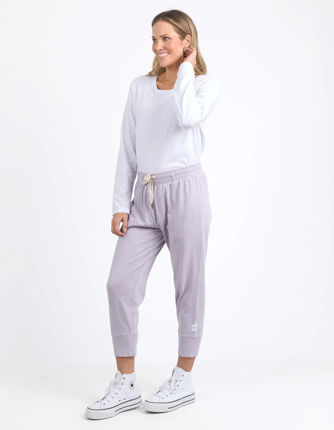 Woman wearing a white sweatshirt and light purple jogger pants on a white background
