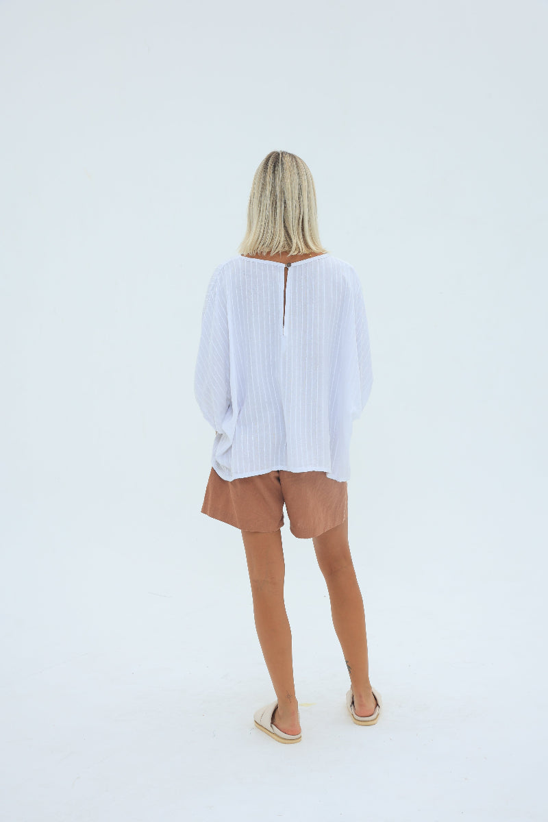 Person wearing a white shirt and brown shorts on a light gray background