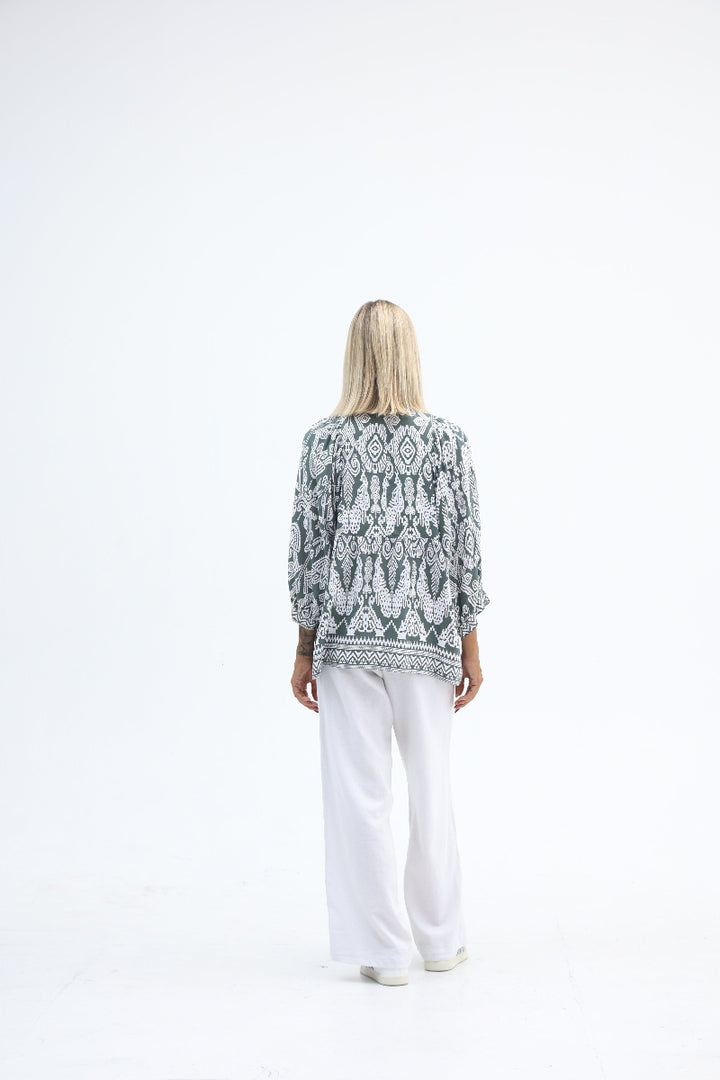Person wearing a patterned top and white pants on a white background