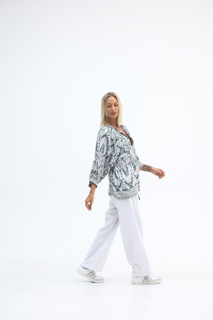 Person wearing a patterned top and white pants on a white background