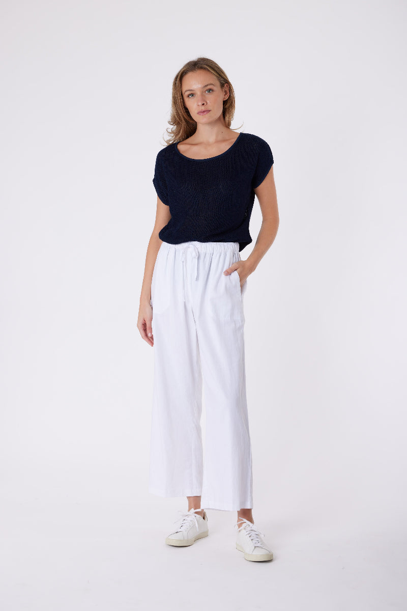 Woman wearing a black top and white pants on a white background