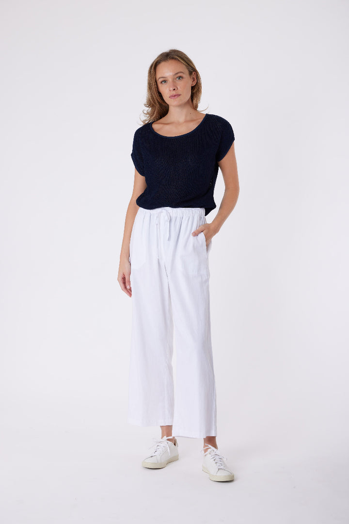 Woman wearing a black top and white pants on a white background