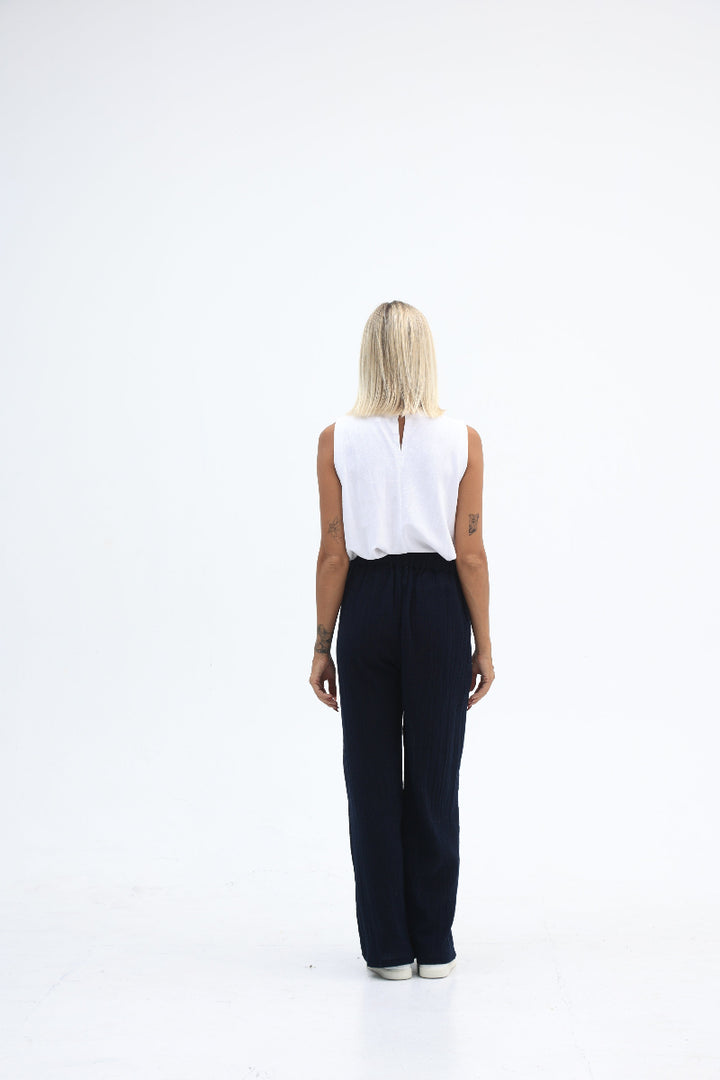 Person wearing a white sleeveless top and black pants on a white background