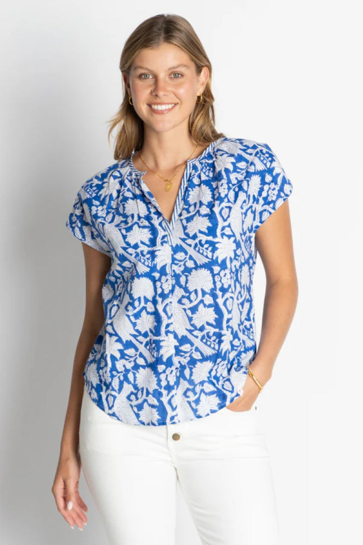 Woman wearing a blue floral blouse with white pants on a plain background