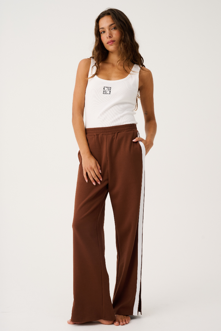 Woman wearing a white tank top and brown pants with a white stripe on a white background