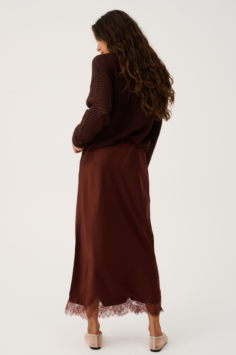 Woman wearing a long brown dress with lace hem on a white background