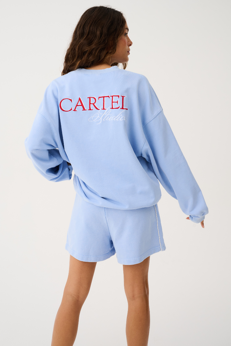 Person wearing a light blue 'Cartel' sweatshirt and shorts on a white background