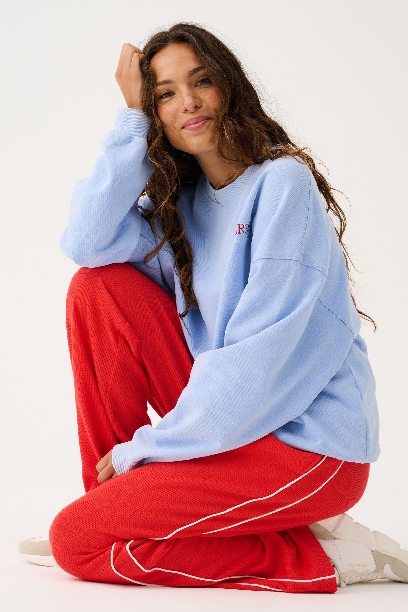 Woman wearing a light blue sweatshirt and red pants sitting on the floor against a white background