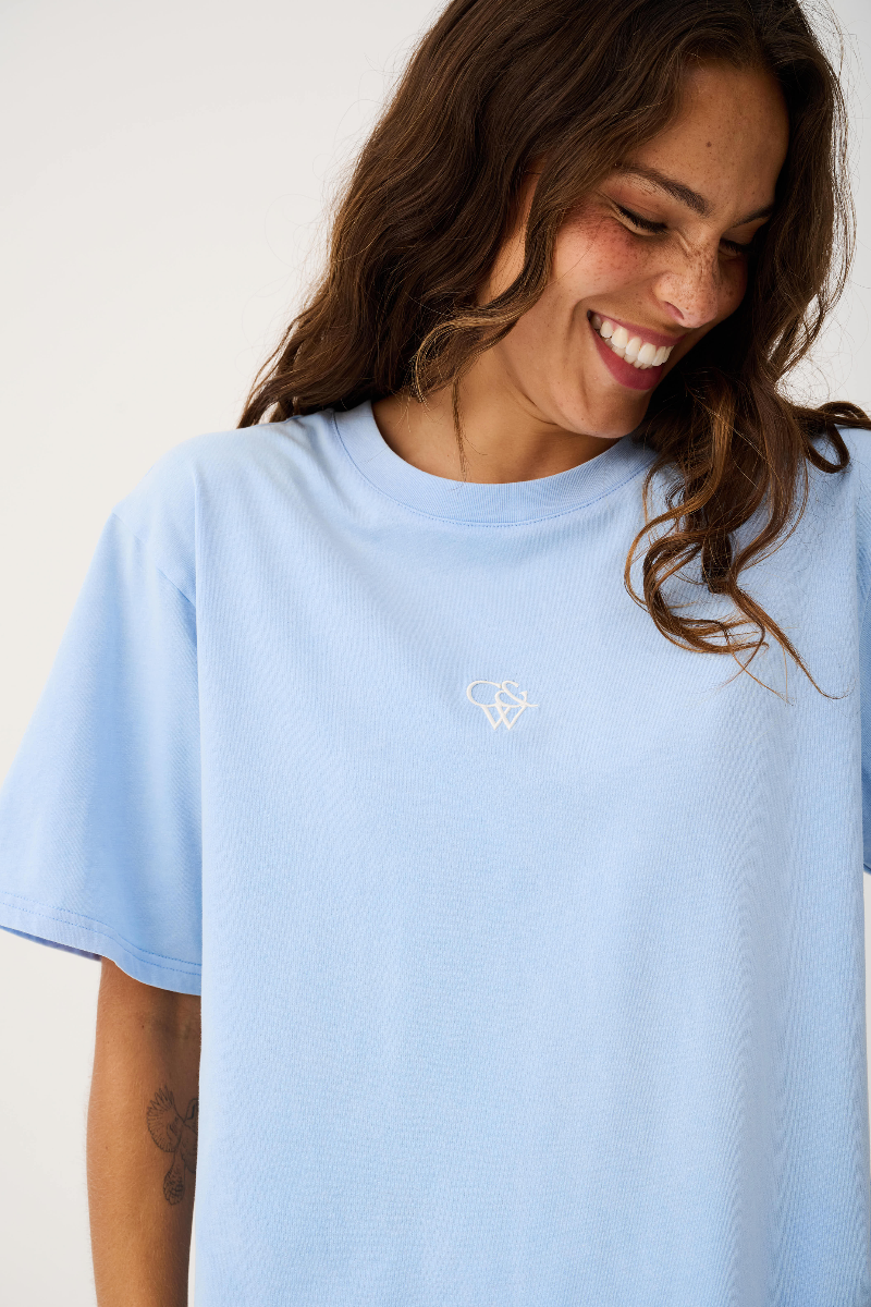 Woman wearing a light blue t-shirt with a small logo on a white background