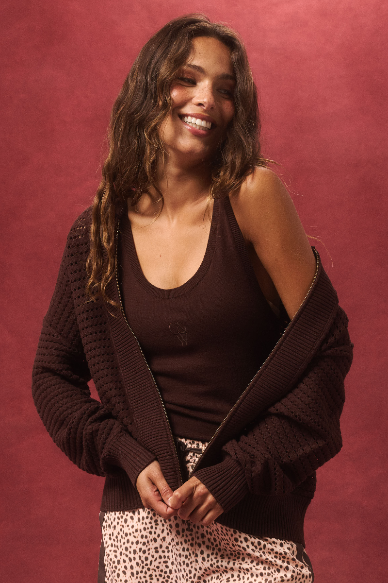 Woman wearing a brown cardigan over a dark top with a red background