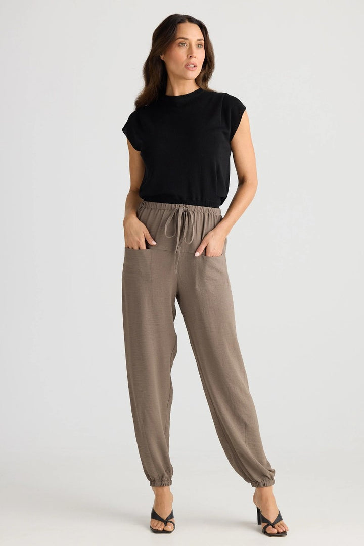 Woman wearing a black top and brown pants on a white background