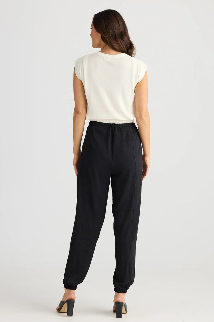 Woman wearing a white top and black pants on a plain background